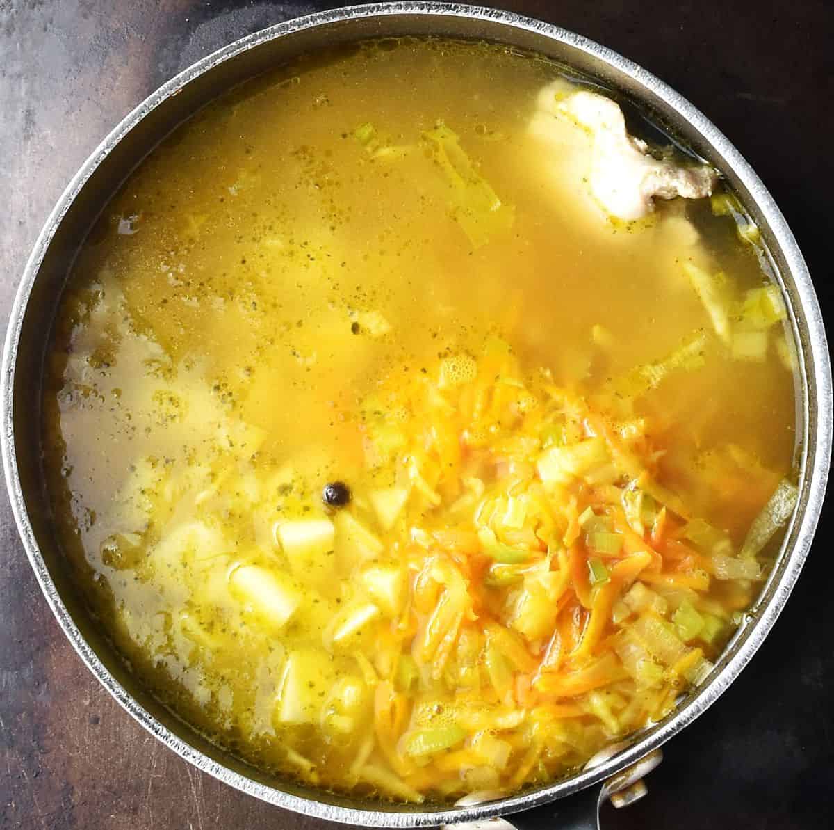 Top down view of Polish pickle soup with vegetables in large black pot.