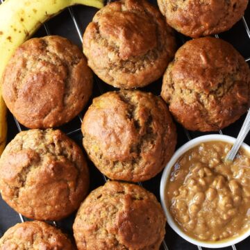 Top down view of cluster of banana peanut butter muffins with ripe banana and crunchy peanut butter in white dish in background.