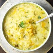 Top down view of Polish dill pickle soup in white bowl with spoon on top of speckled plate.