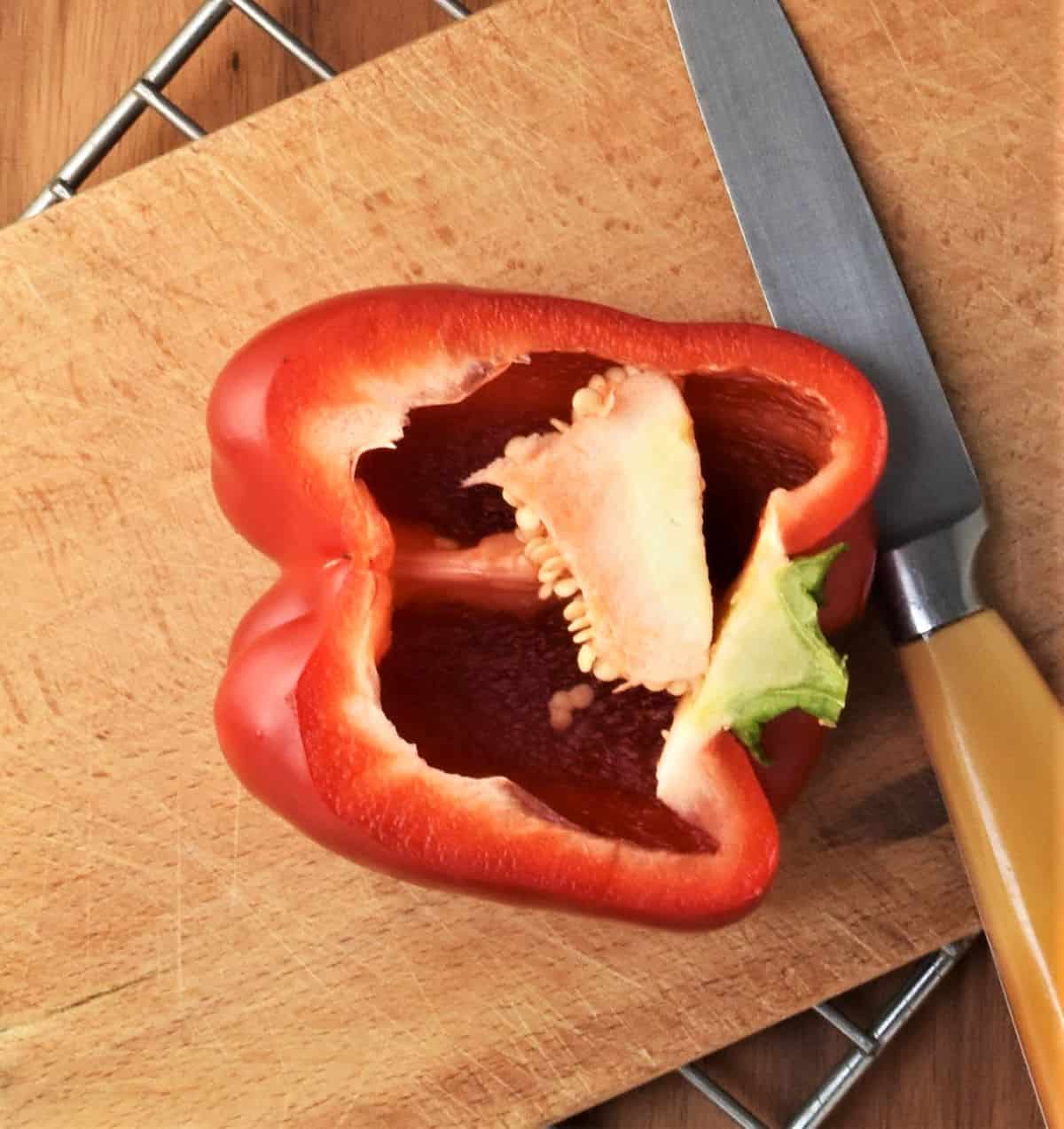 Halved red pepper on cutting board with small knife.