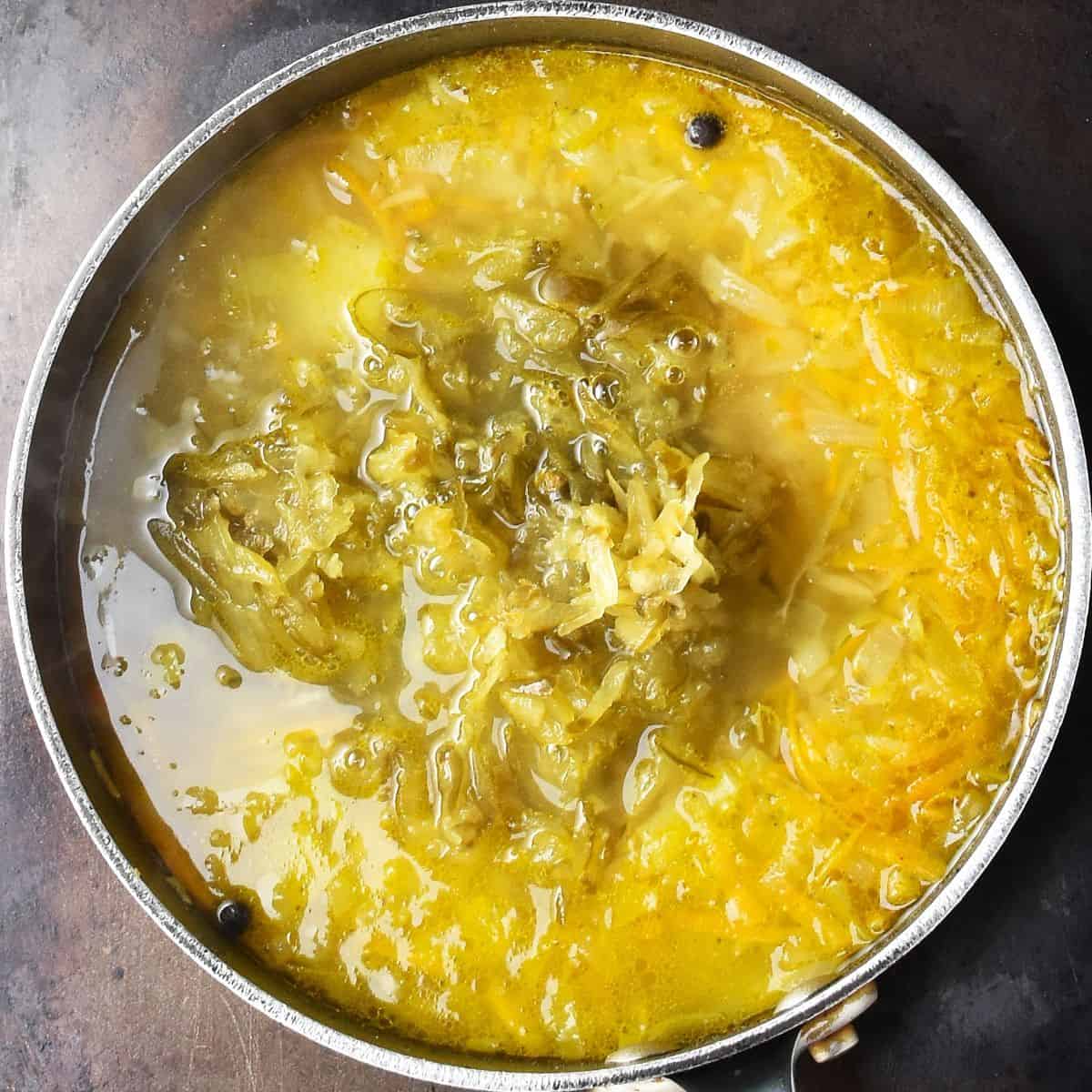 Top down view of shredded dill pickles in soup in large pot.