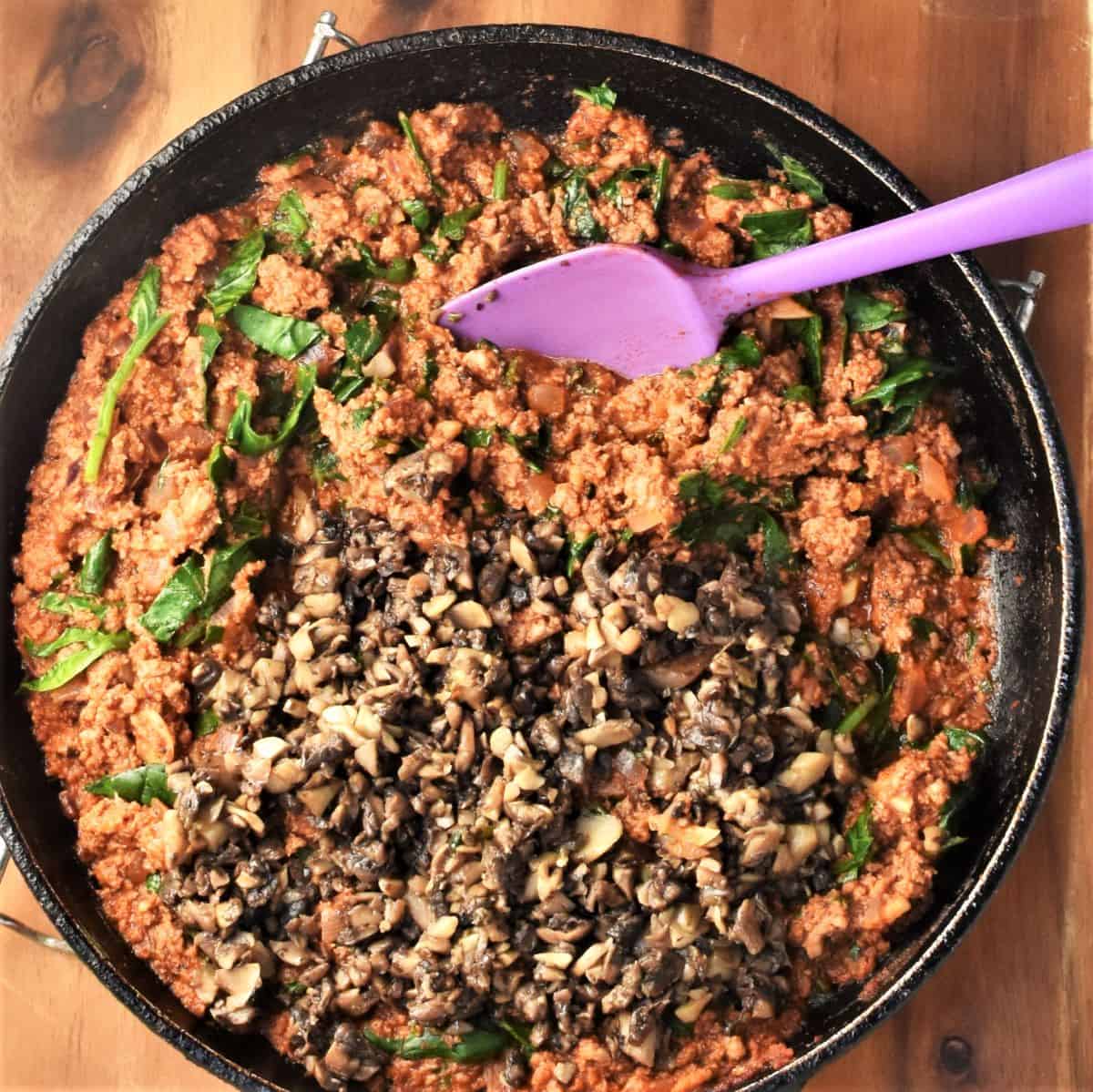 Meat mixture with mushrooms in pan with purple spatula.