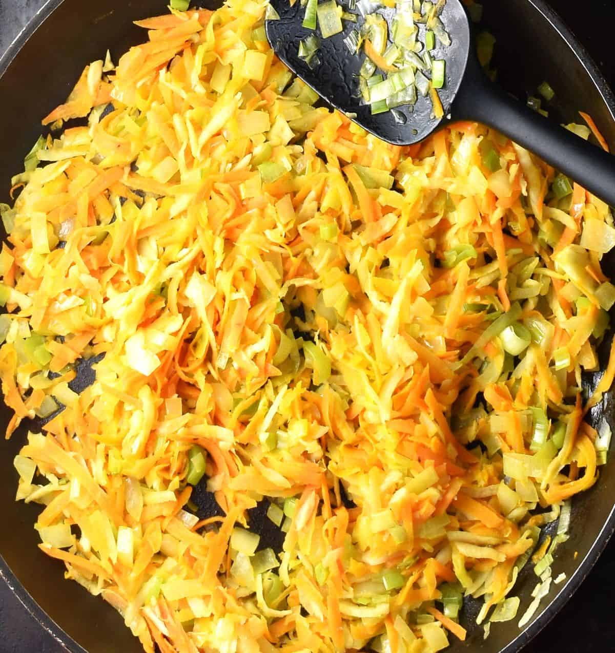 Top down view of shredded vegetables in large pan with black spatula.
