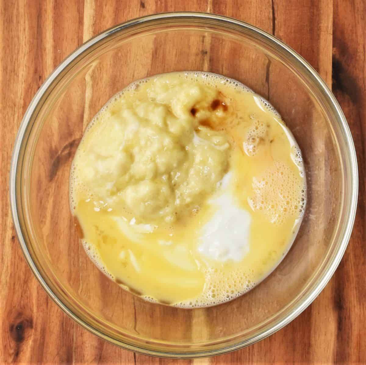 Mashed banana and other wet pancake ingredients in bowl.