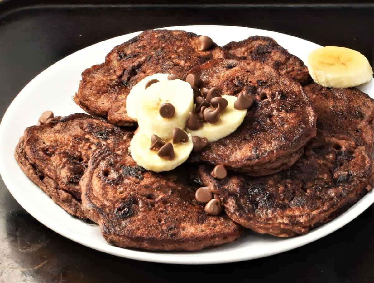 Side view of banana and chocolate pancakes on top of plate with sliced banana.