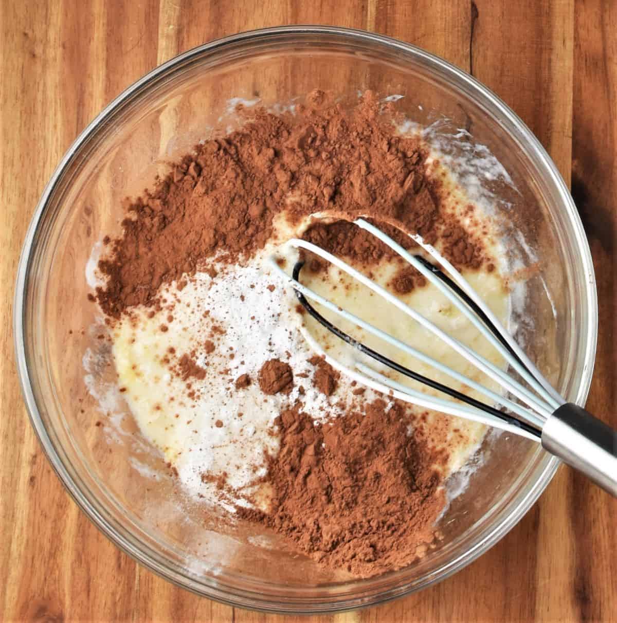 Wet pancake ingredients and cacao in bowl with whisk.