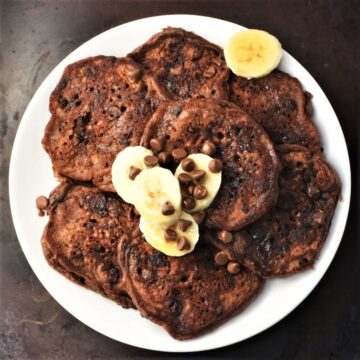 Top down view of chocolate banana pancakes on white plate with banana slices.