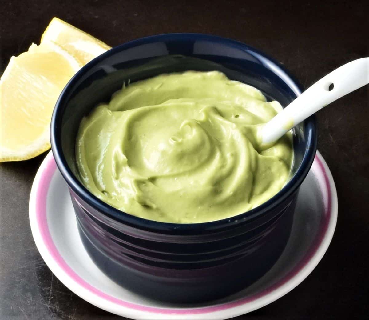 Side view of avocado mayonnaise in blue bowl with white spoon.