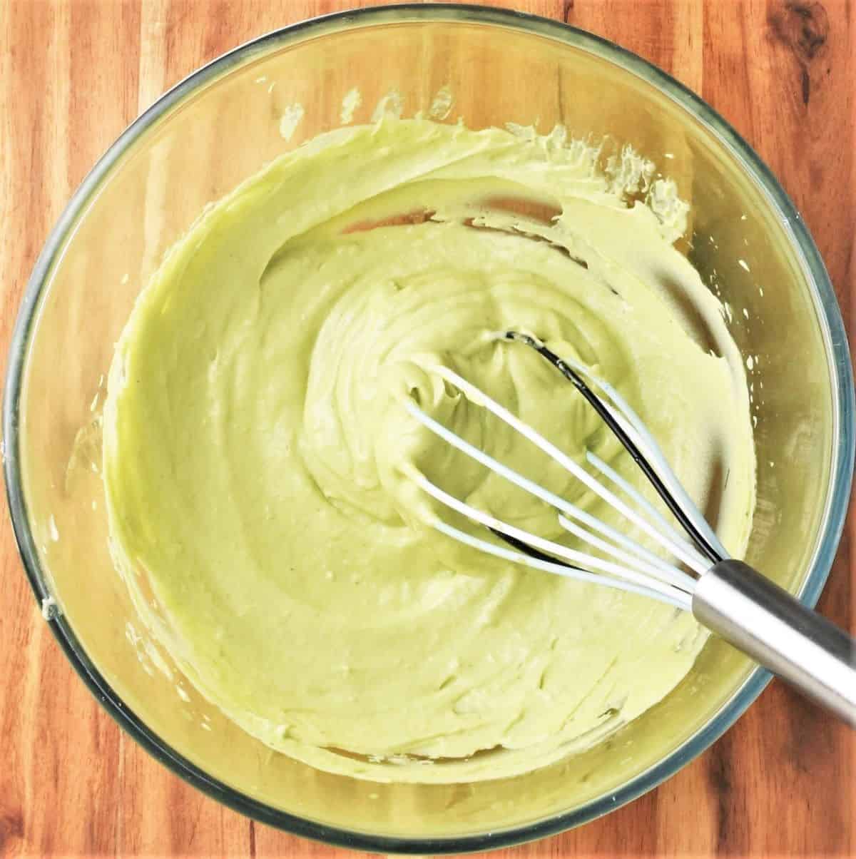 Creamy green coloured mayonnaise in bowl with whisk.