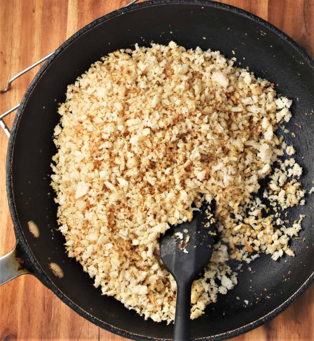Golden breadcrumbs in pan with black spatula.