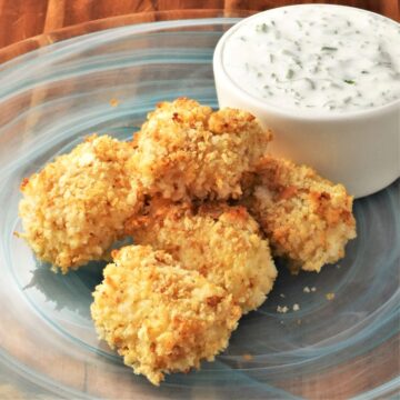 Side view of breaded fish nuggets on top of blue plate with yogurt sauce.
