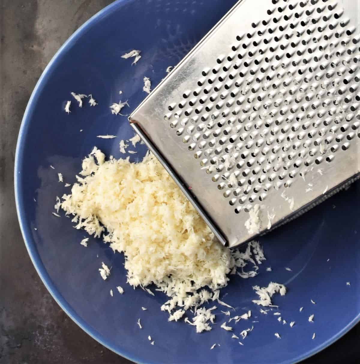 Finely grated fresh horseradish in blue bowl with box grater.