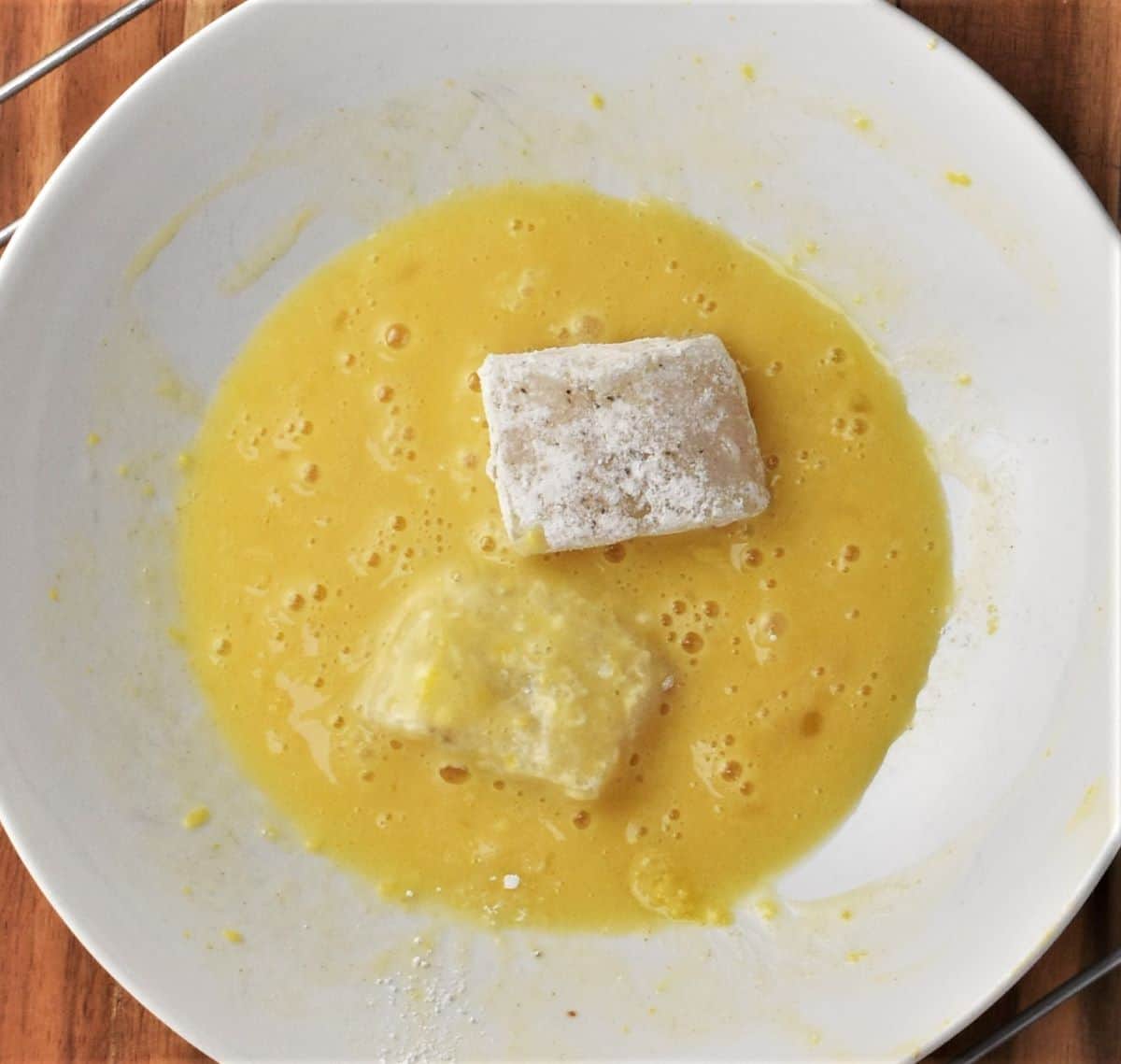 Egg mixture with fish pieces in white bowl.