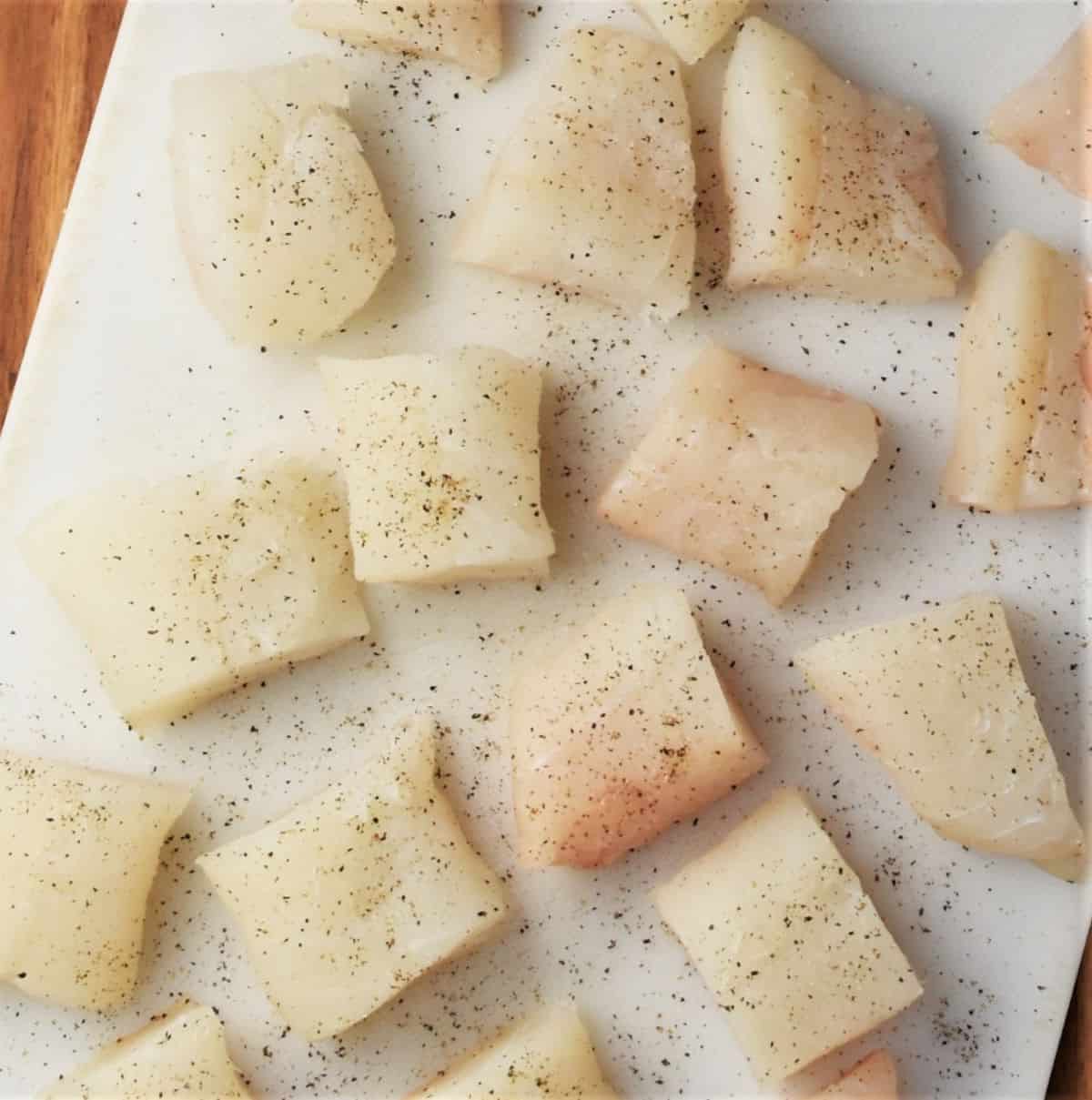 Seasoned fish chunks on top of white cutting board.