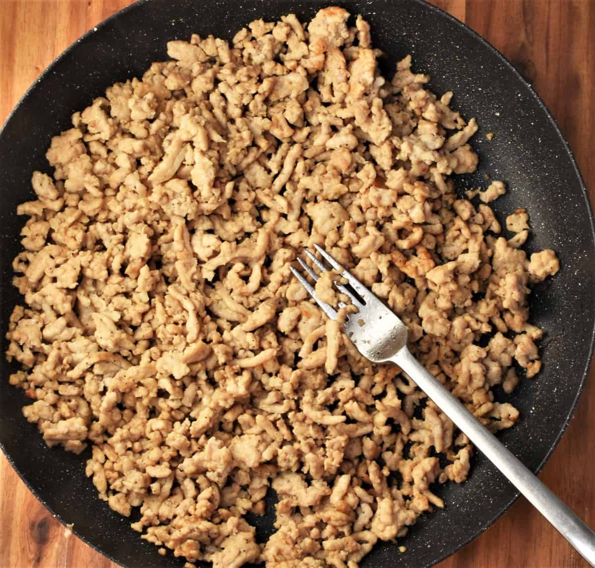 Browning ground chicken in pan with fork.