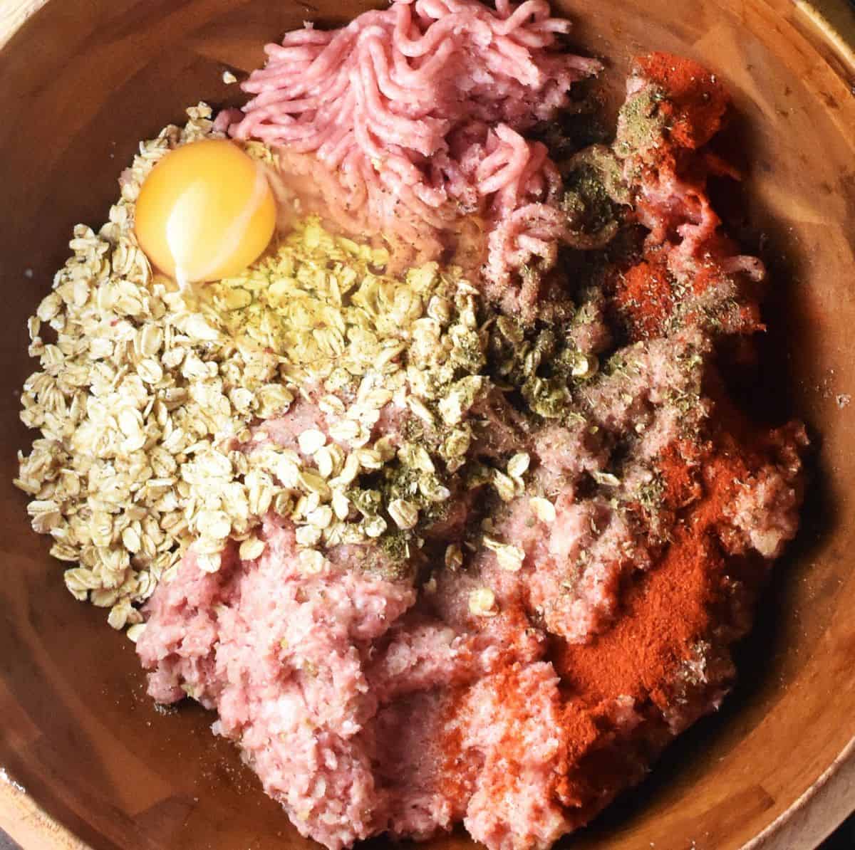 Assembled ingredients for meatloaf with oats in large wooden bowl.