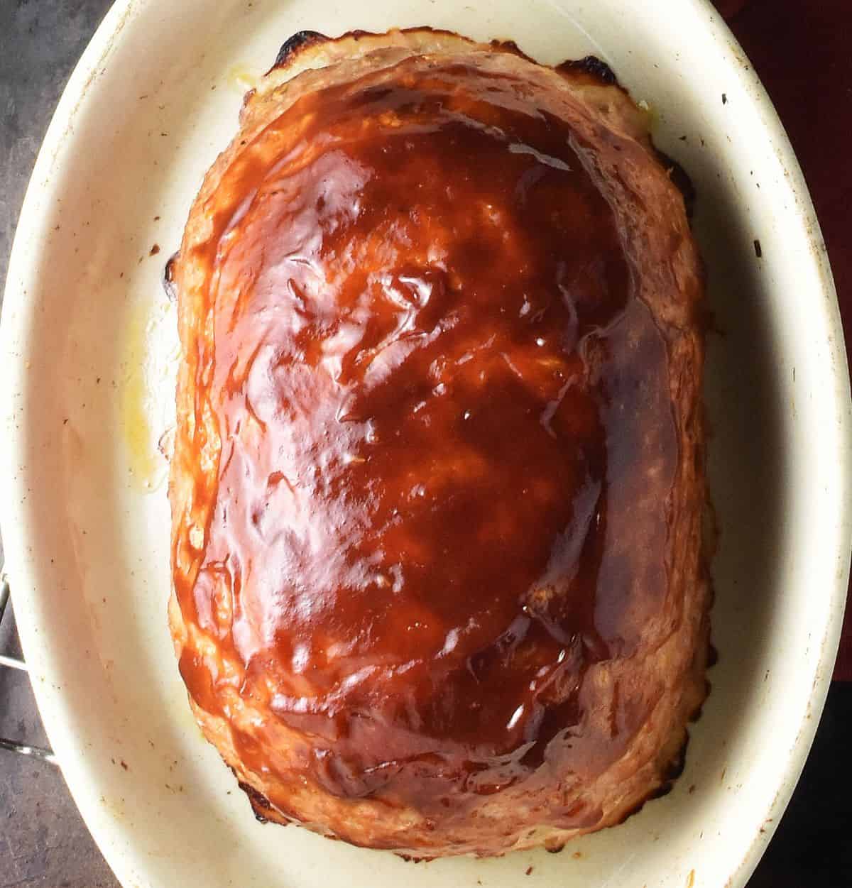 Top down view of meatloaf with glaze on top in oval white dish.