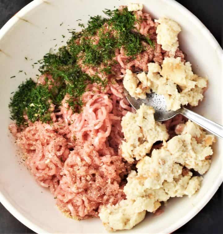 Top down view of ground chicken and herbs in white bowl.