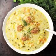 Top down view of chicken meatball soup in white bowl with spoon.