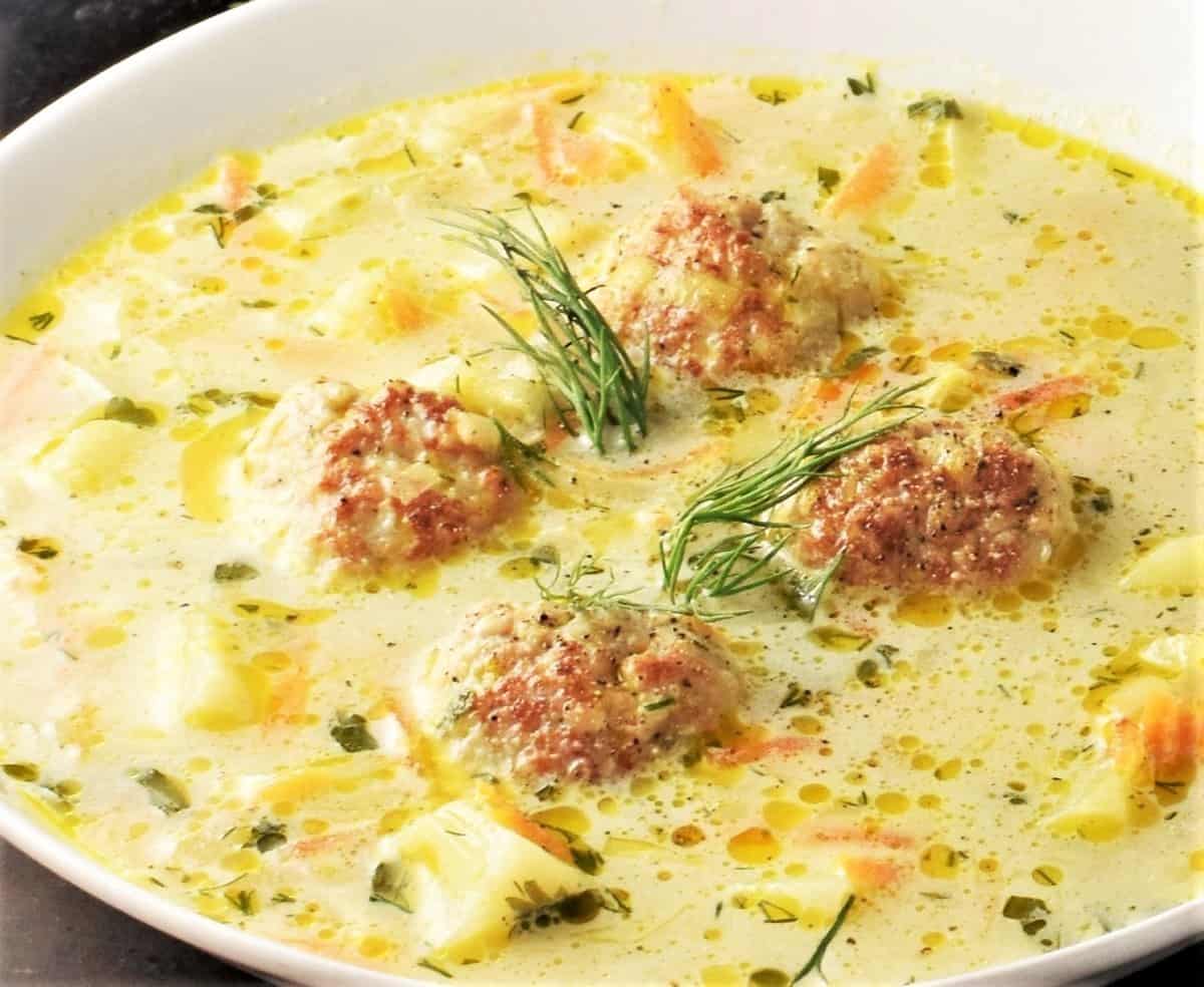 Side view of soup with chicken meatballs and vegetables in white bowl.