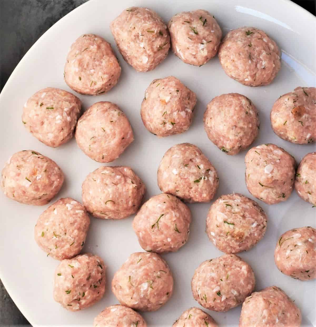 Raw chicken meatballs on white plate.