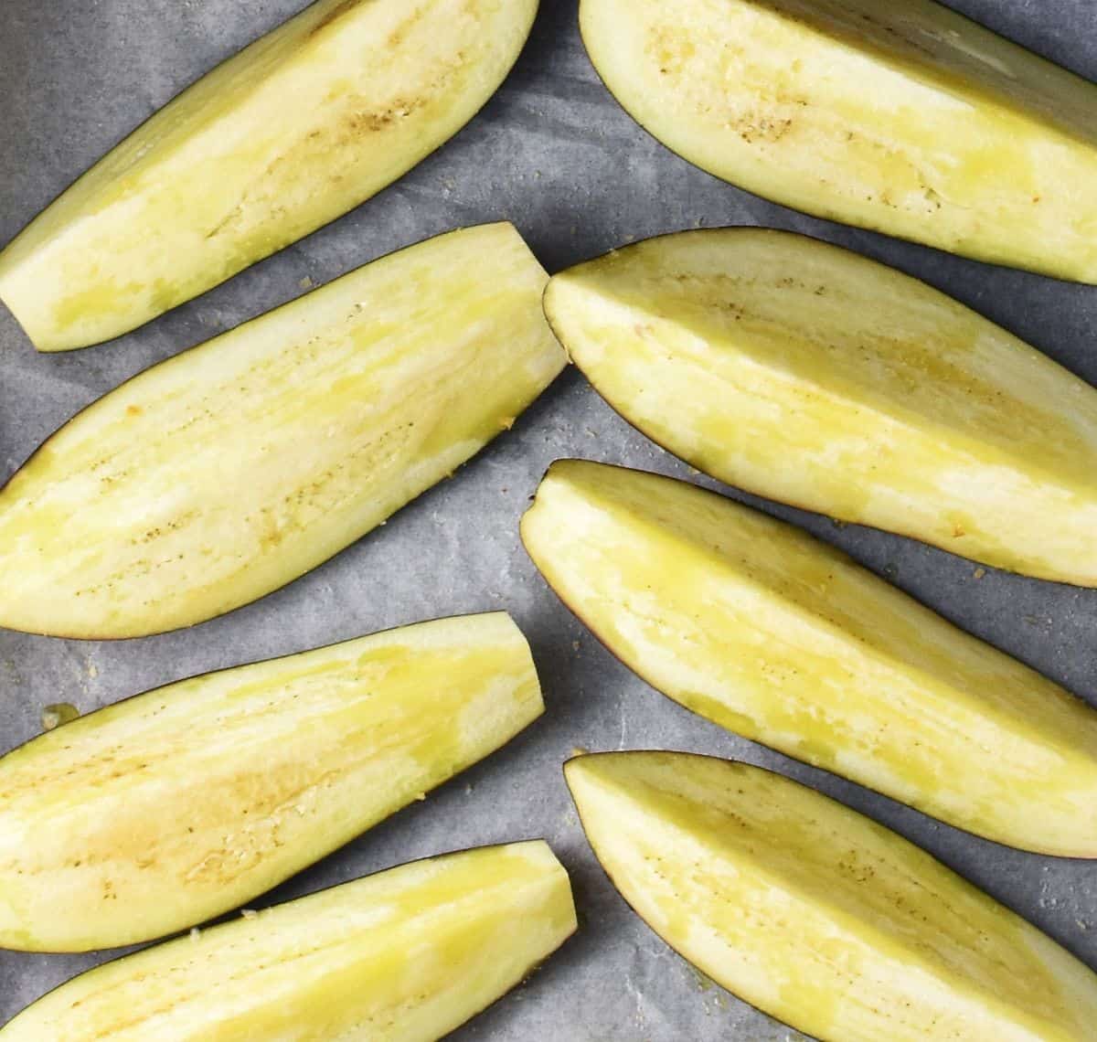Top down view of 8 long eggplant strips on top of parchment.
