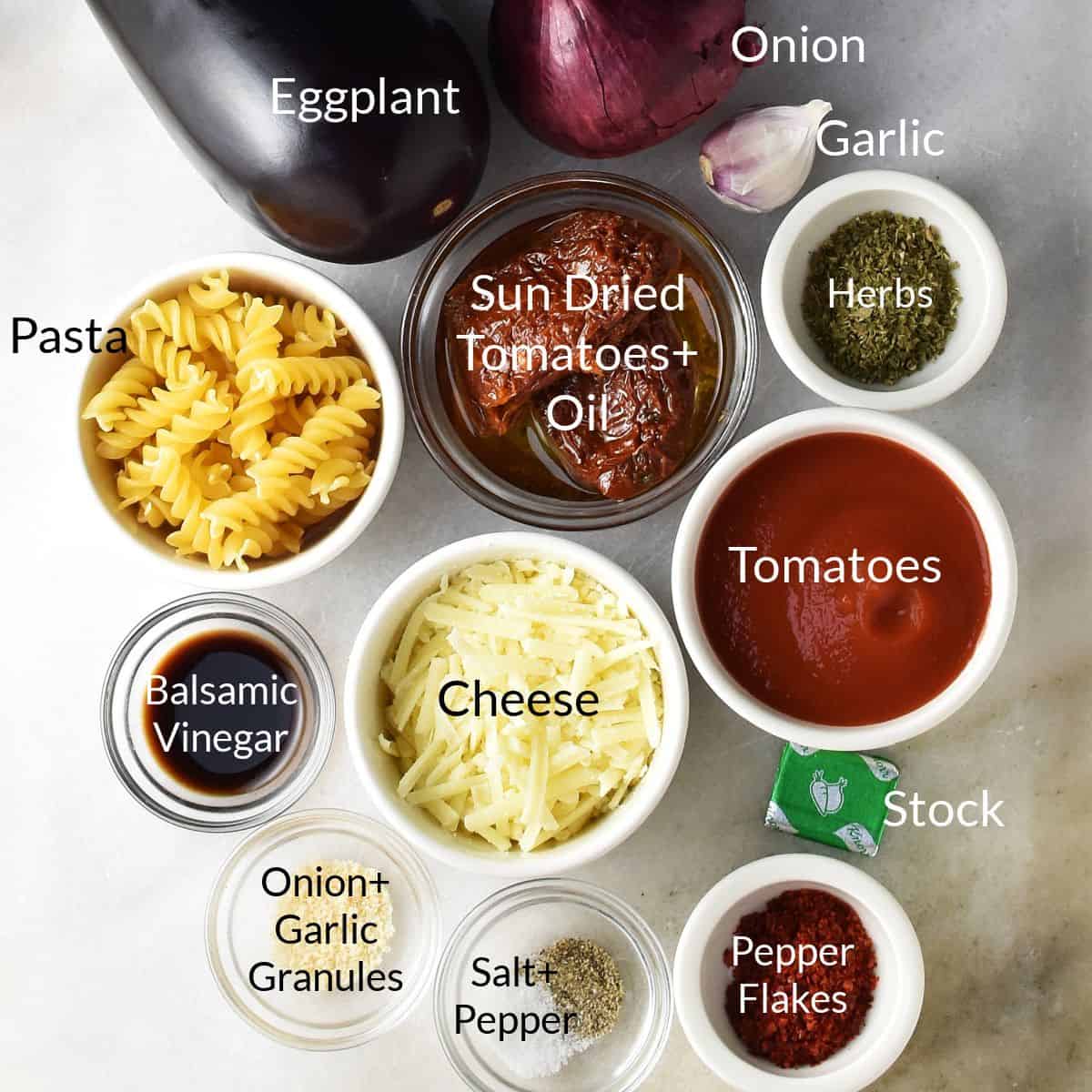 Top down view of ingredients for roasted eggplant pasta bake in individual dishes on marble top.