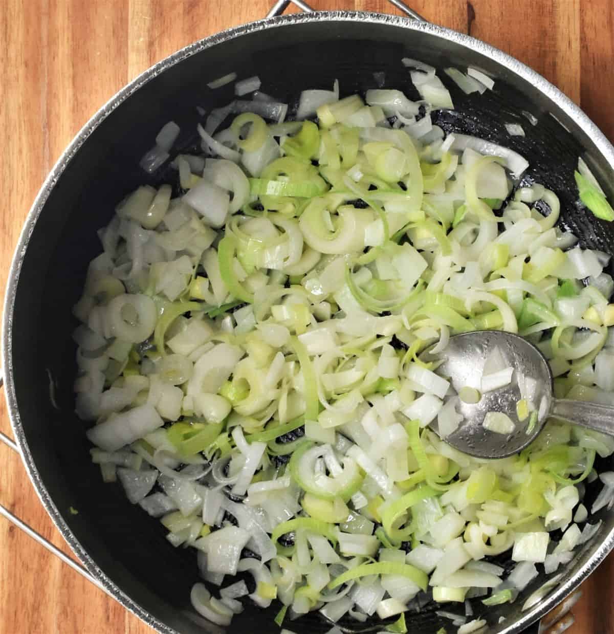 Chopped onion and leek in large pot with spoon.