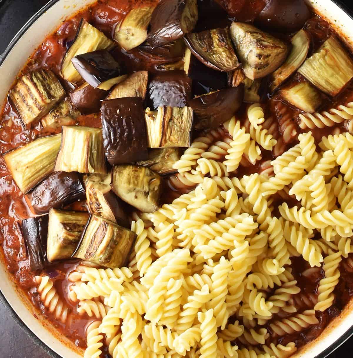 Fusilli pasta with chopped roasted eggplant and tomato sauce in shallow pan.