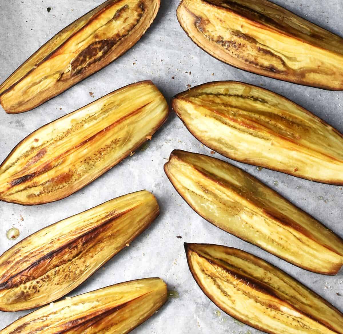Top down view of lightly browned, roasted strips of eggplant on top of parchment.