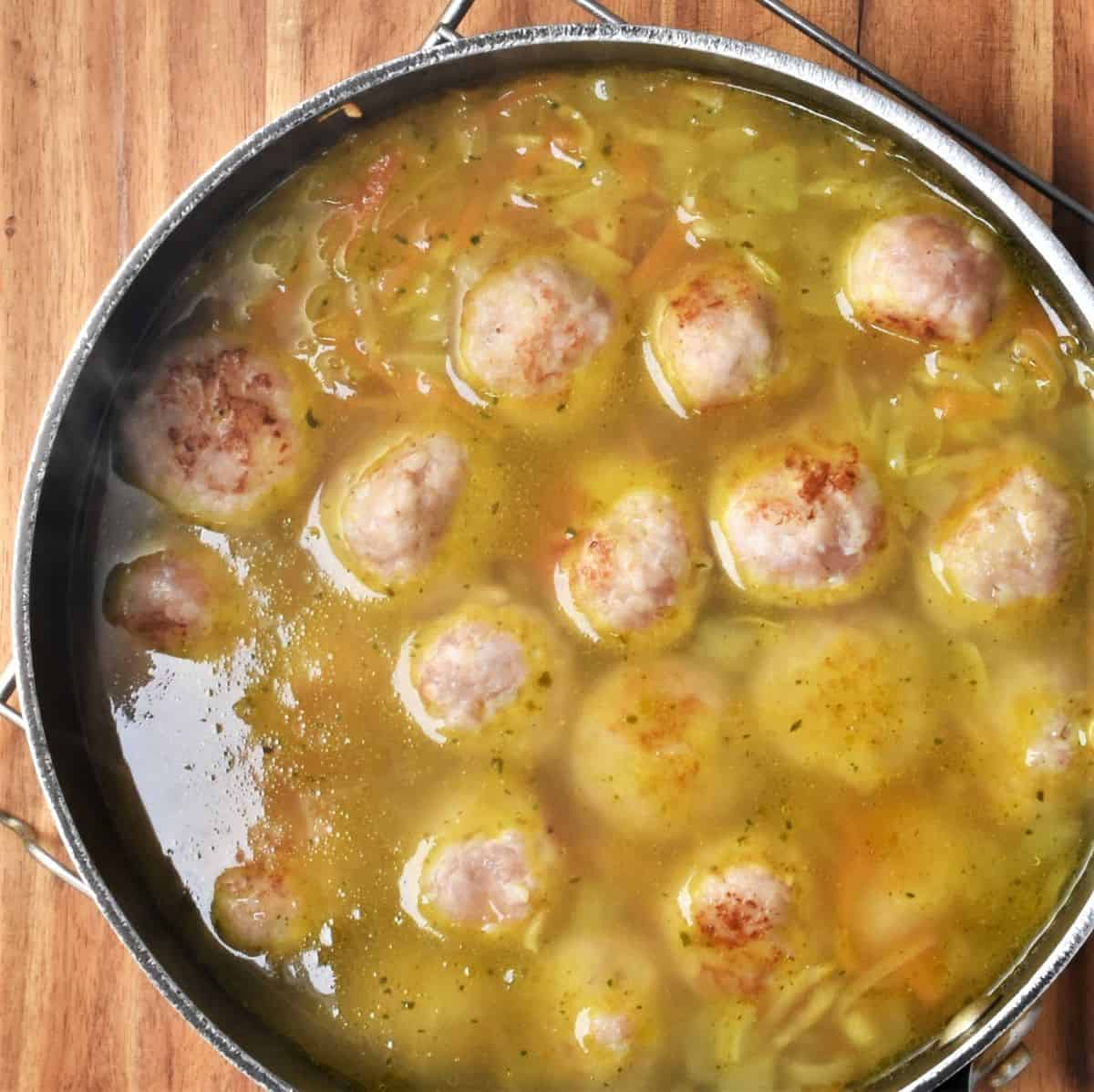 Top down view of vegetable soup with chicken meatballs in large pot.