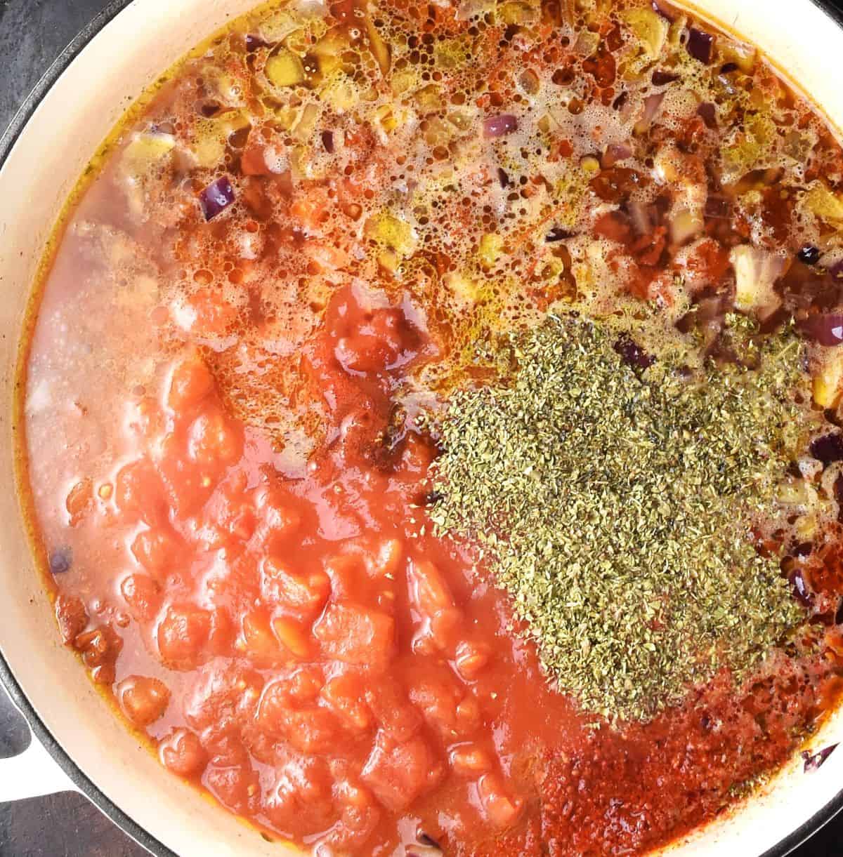Top down view of chopped tomatoes with stock and herbs in shallow white pan.