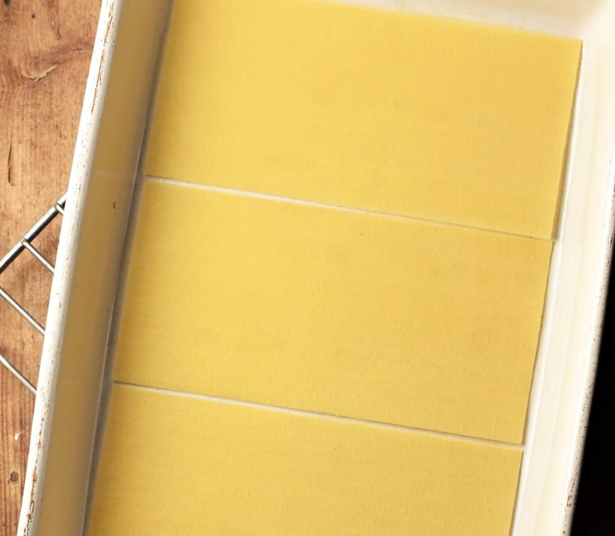 Top down view of 3 lasagne noodles lining bottom of dish.