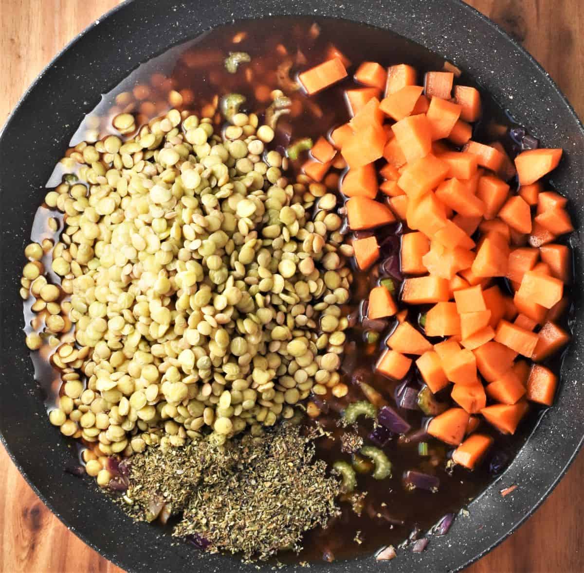 Cooking lentils with carrot and stock in large shallow pan.