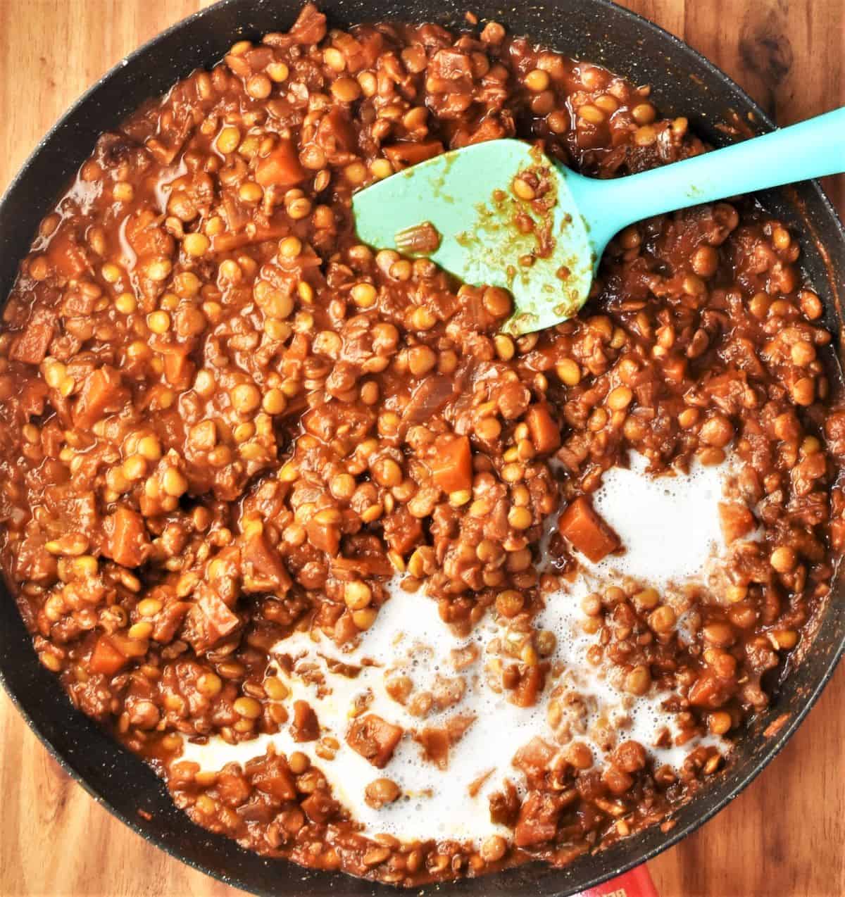 Thick lentil ragu sauce with cream in large shallow pan with blue spoon.