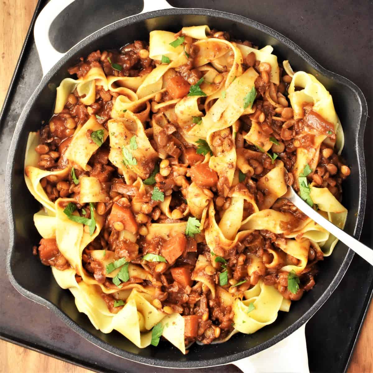 Lentil ragu sauce with pappardelle pasta in skillet with fork.