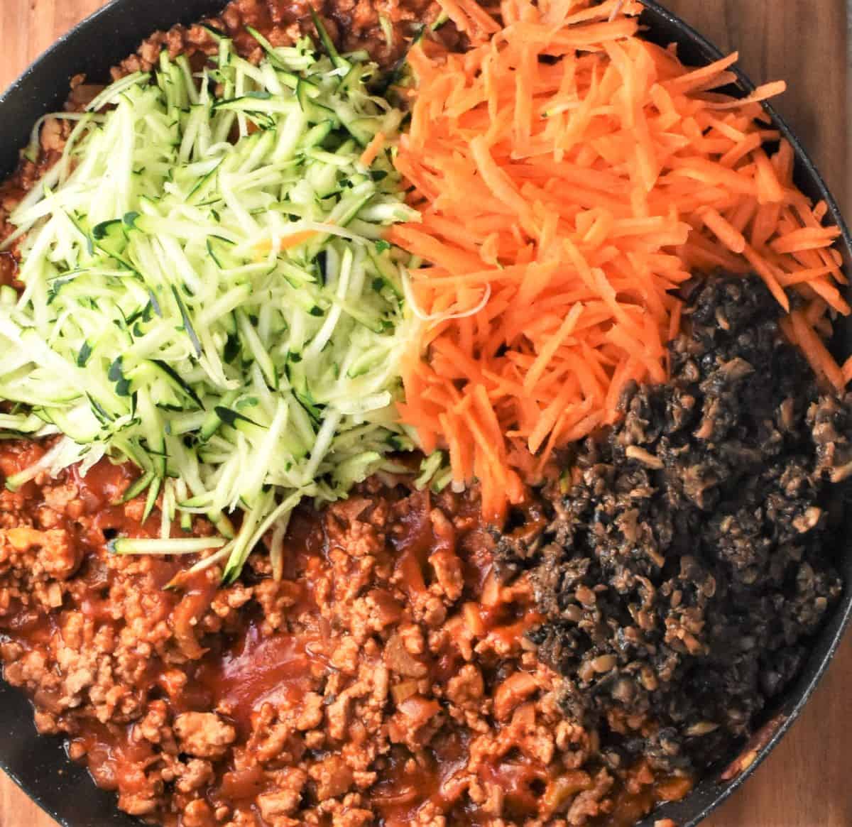 Assembling lasagna filling with turkey, sauce and vegetables in large pan.