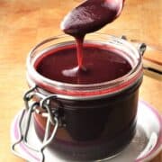 Side view of creamy blackberry coulis in jar with spoon over it.
