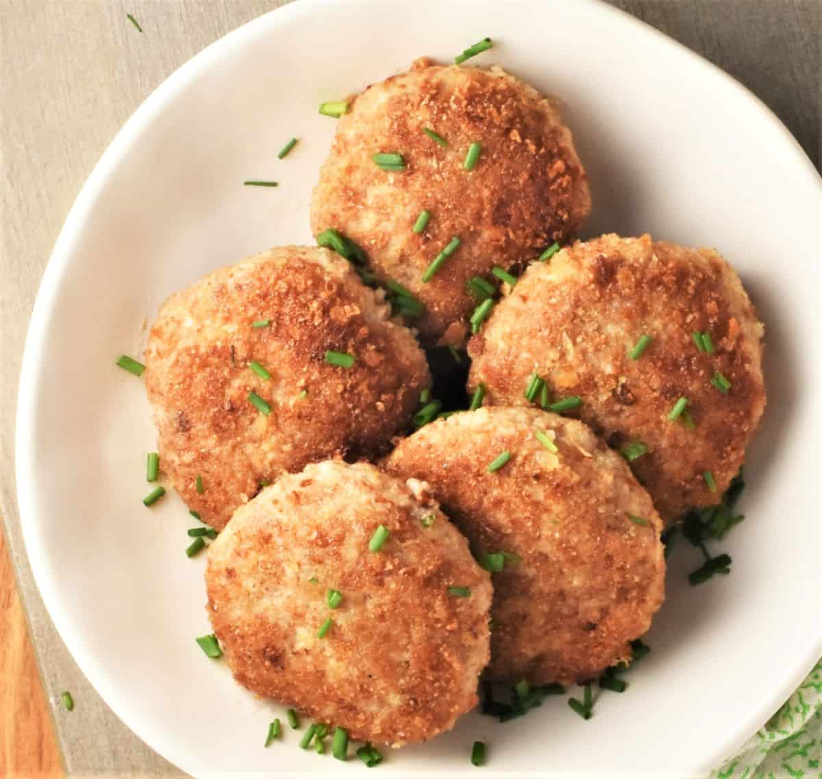 Top down view of 5 breaded Polish patties in white bowl with garnish of chives.