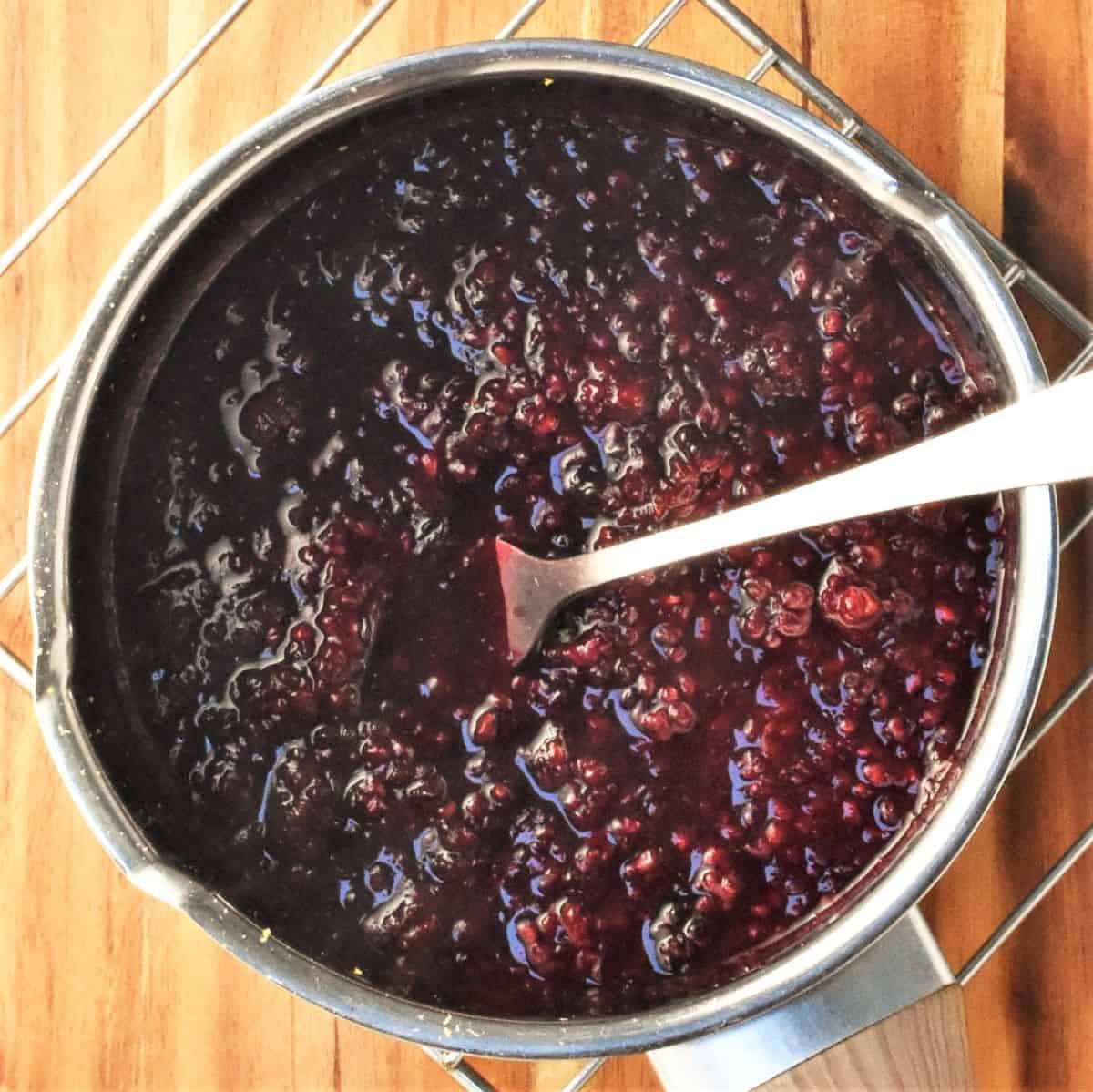 Blackberry coulis mixture with mashed up fruit in pot with spoon.