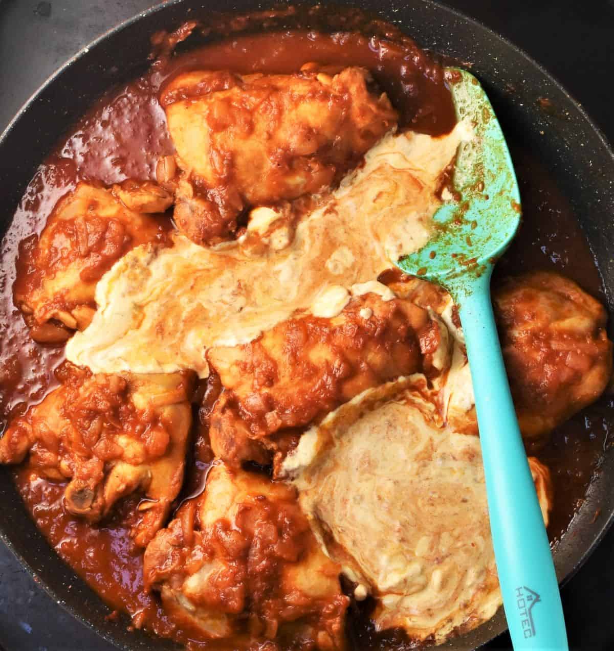 Chicken paprikash with sour cream in large pan with blue spoon.