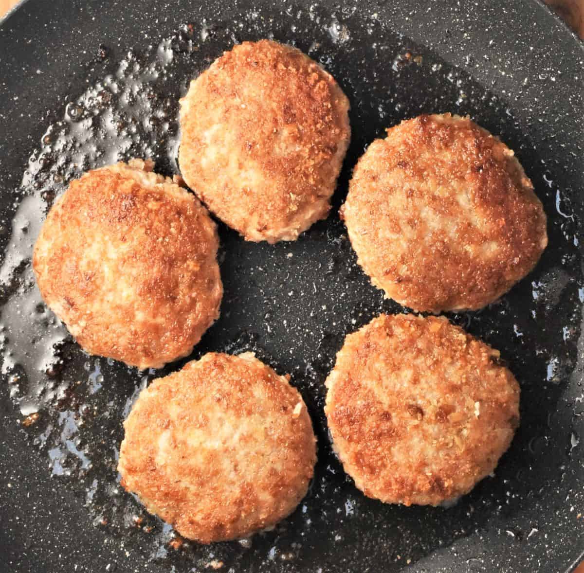 Frying 5 Polish burgers in black pan with oil.