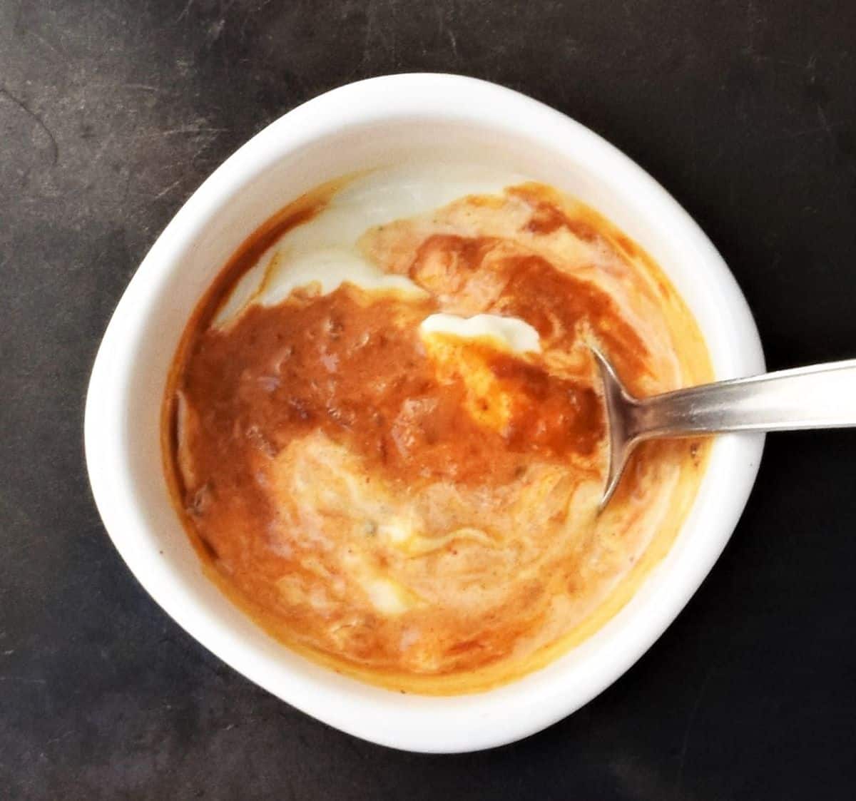 Sour cream with paprika sauce in white bowl with spoon.