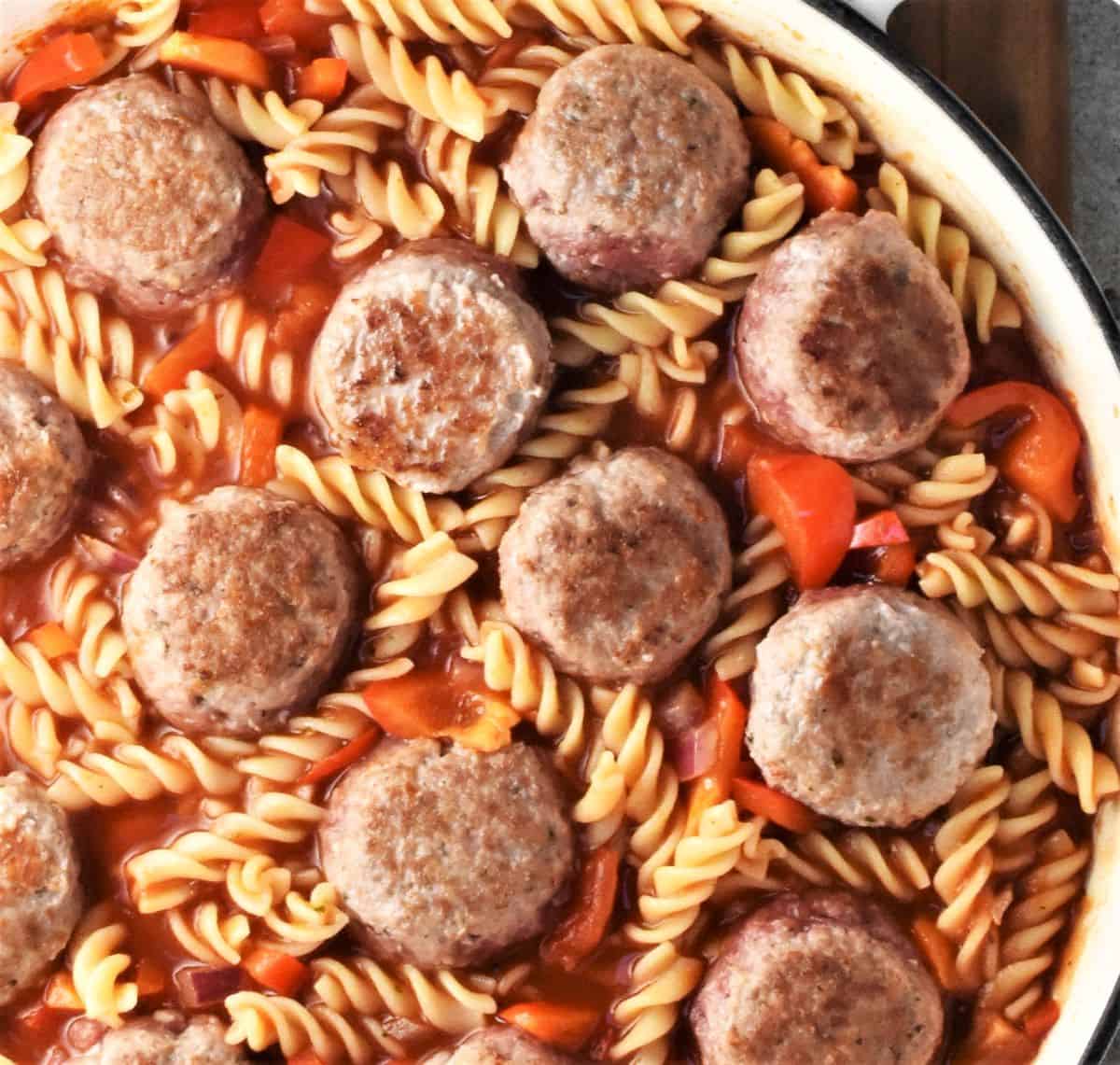 Assembling meatball and pasta bake in large shallow pan.