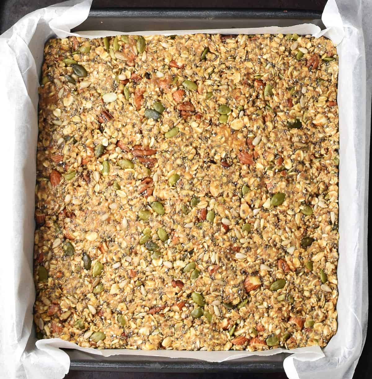 Top down view of homemade granola bar mixture packed in pan with parchment paper.