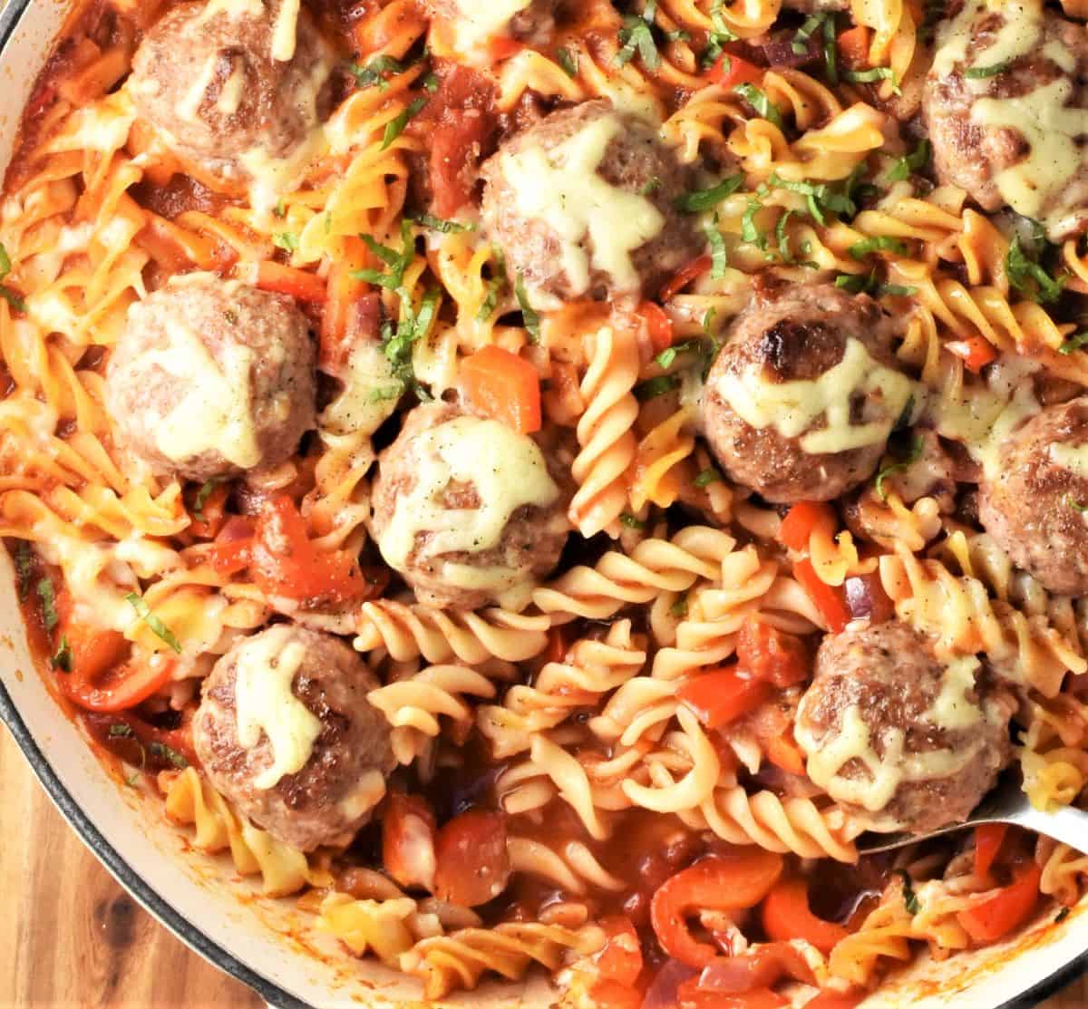 Top down partial view of meatball pasta casserole with spoon in shallow dish.