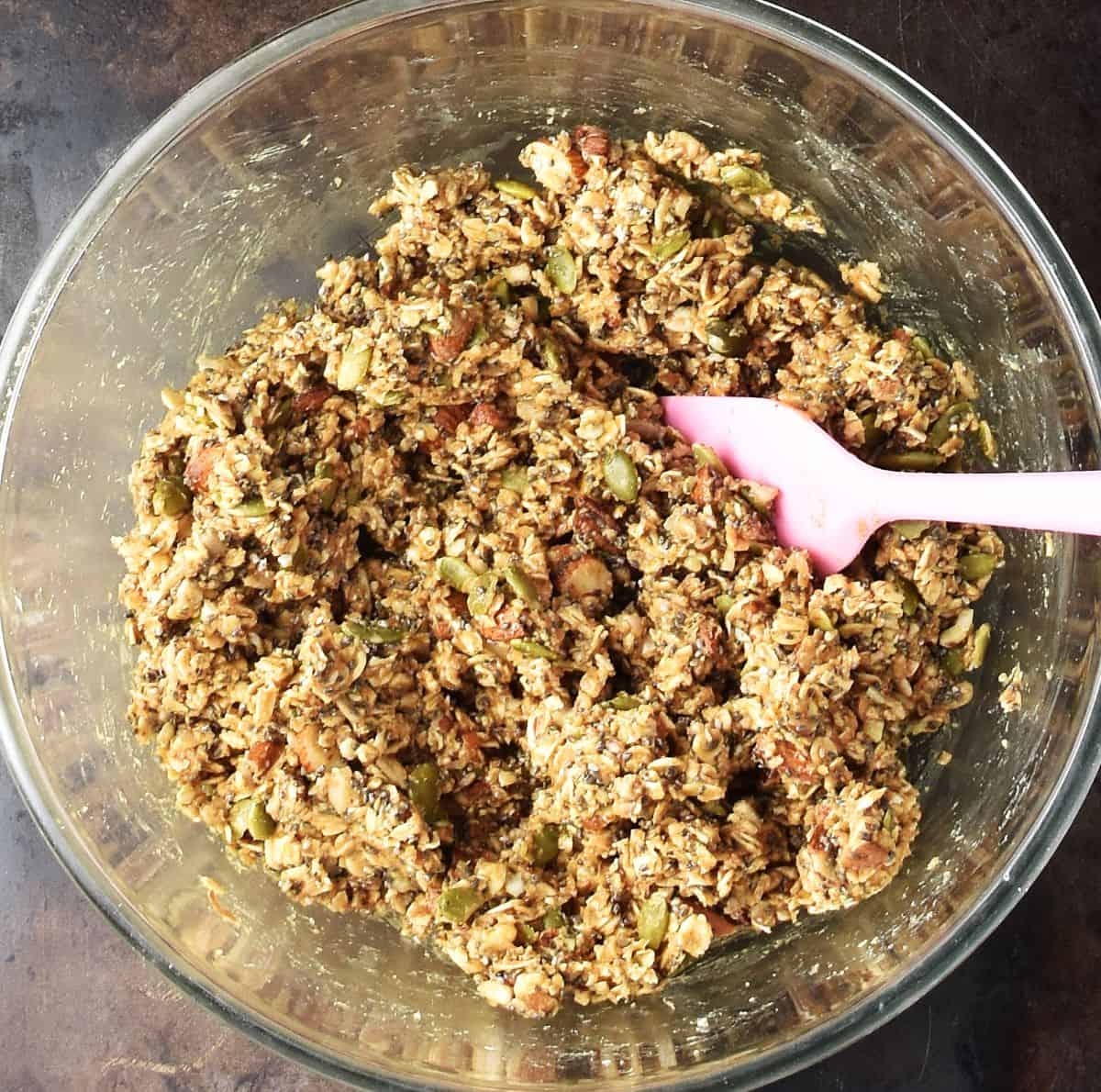 Protein granola bar batter in glass bowl with pink spatula.