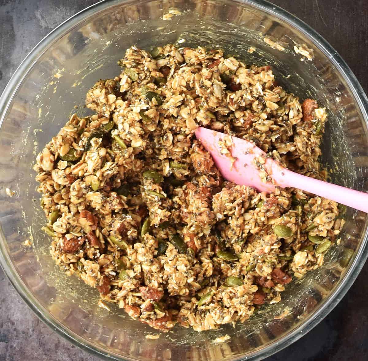 Top down view of homemade protein granola bar mixture in glass bowl with pink spatula.