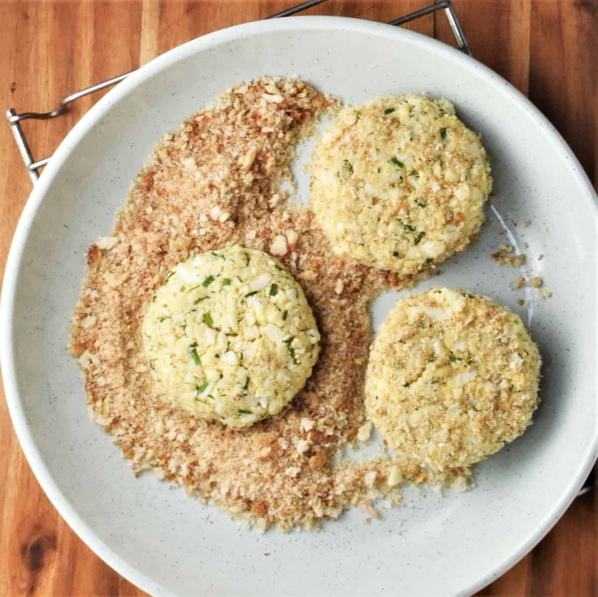 3 breaded egg patties in bowl with breadcrumbs.