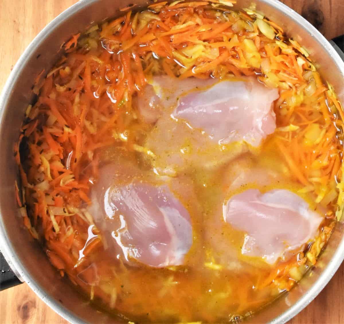 3 skinless chicken thighs with vegetables and stock in pot.